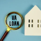 “VA loans” shown in a magnifying glass placed next to a cream-colored wooden 2D home.